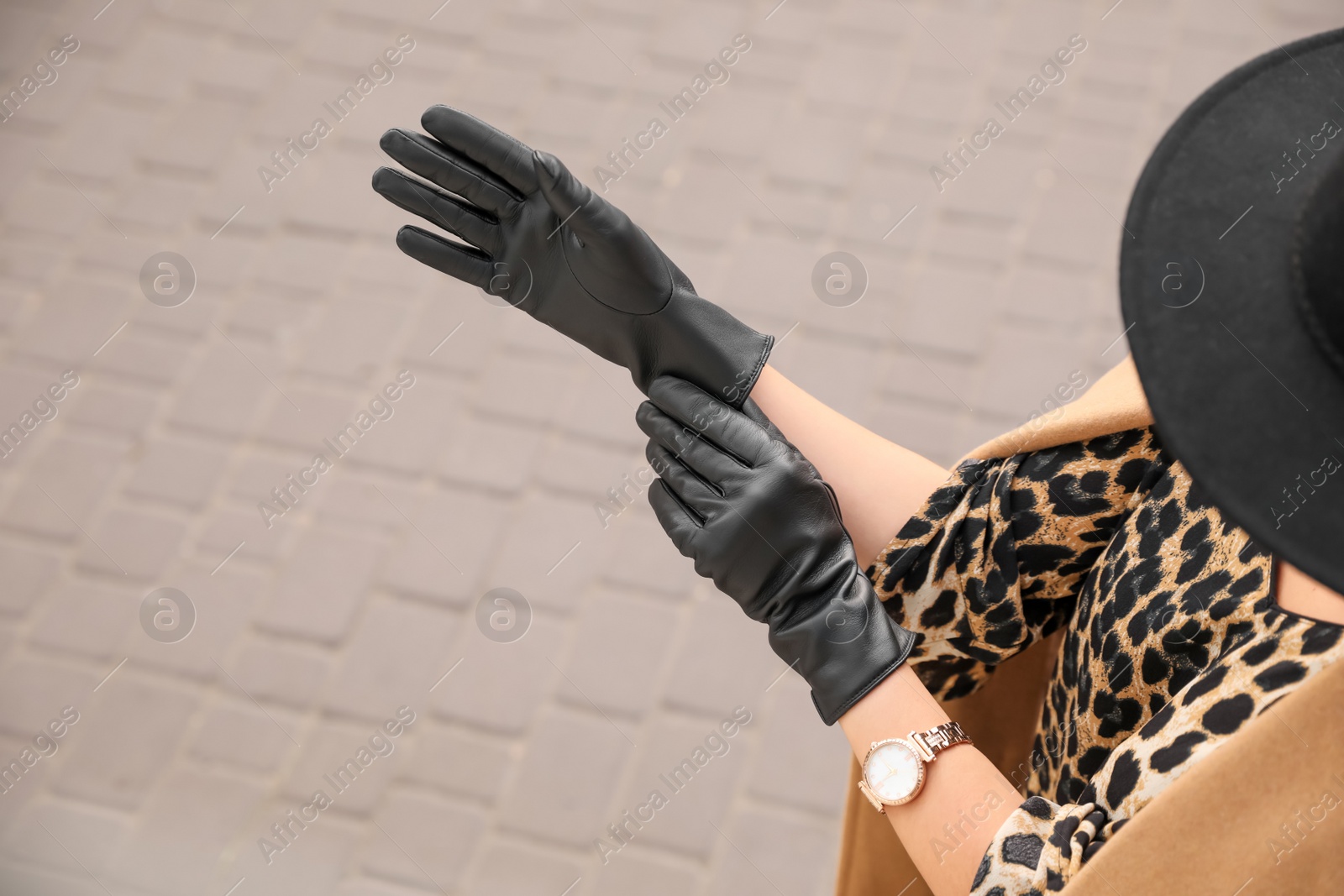 Photo of Young woman putting on stylish black leather gloves outdoors, closeup