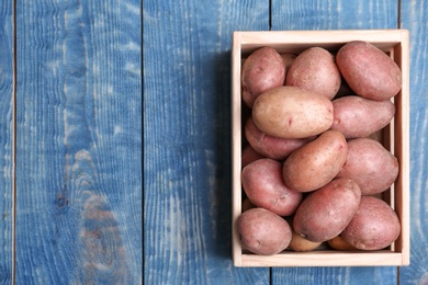 Photo of Crate with fresh ripe organic potatoes on wooden background, top view