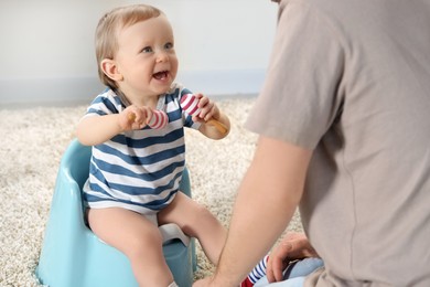 Photo of Father training his child to sit on baby potty indoors