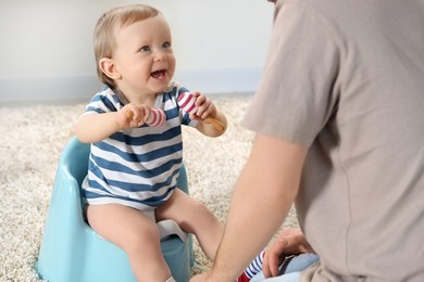 Father training his child to sit on baby potty indoors