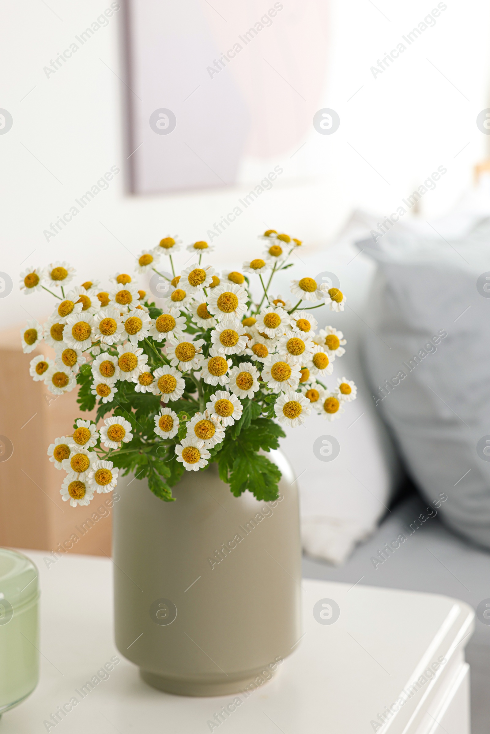 Photo of Beautiful bouquet of chamomile flowers on white nightstand in bedroom. Interior element