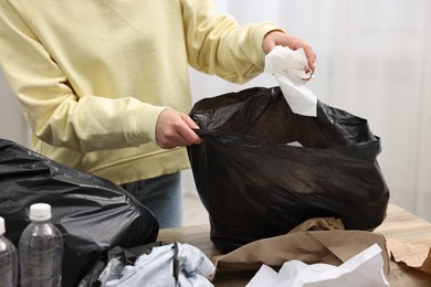 Photo of Woman with plastic bag separating garbage in room, closeup