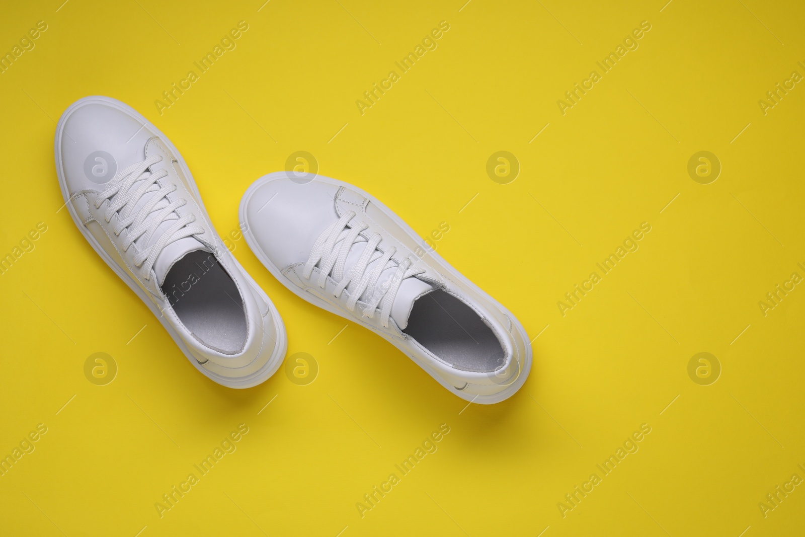 Photo of Pair of stylish white sneakers on yellow background, top view. Space for text