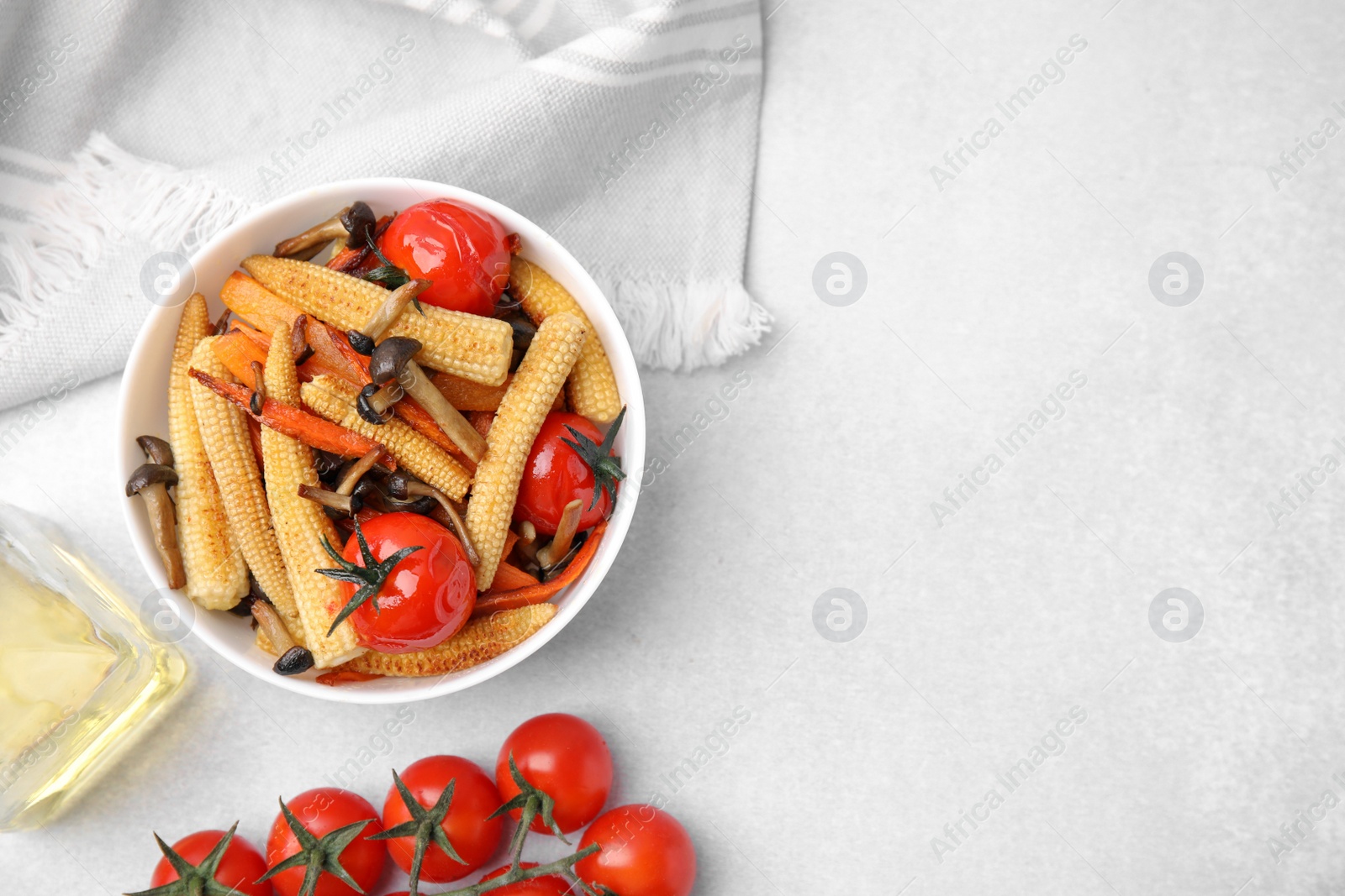 Photo of Tasty roasted baby corn with tomatoes and mushrooms on white table, flat lay. Space for text