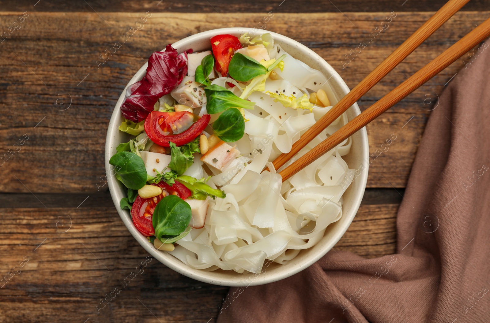 Photo of Tasty cooked rice noodles with chicken and vegetables on wooden table, top view