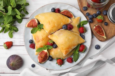 Photo of Delicious samosas with figs and berries on white wooden table, flat lay