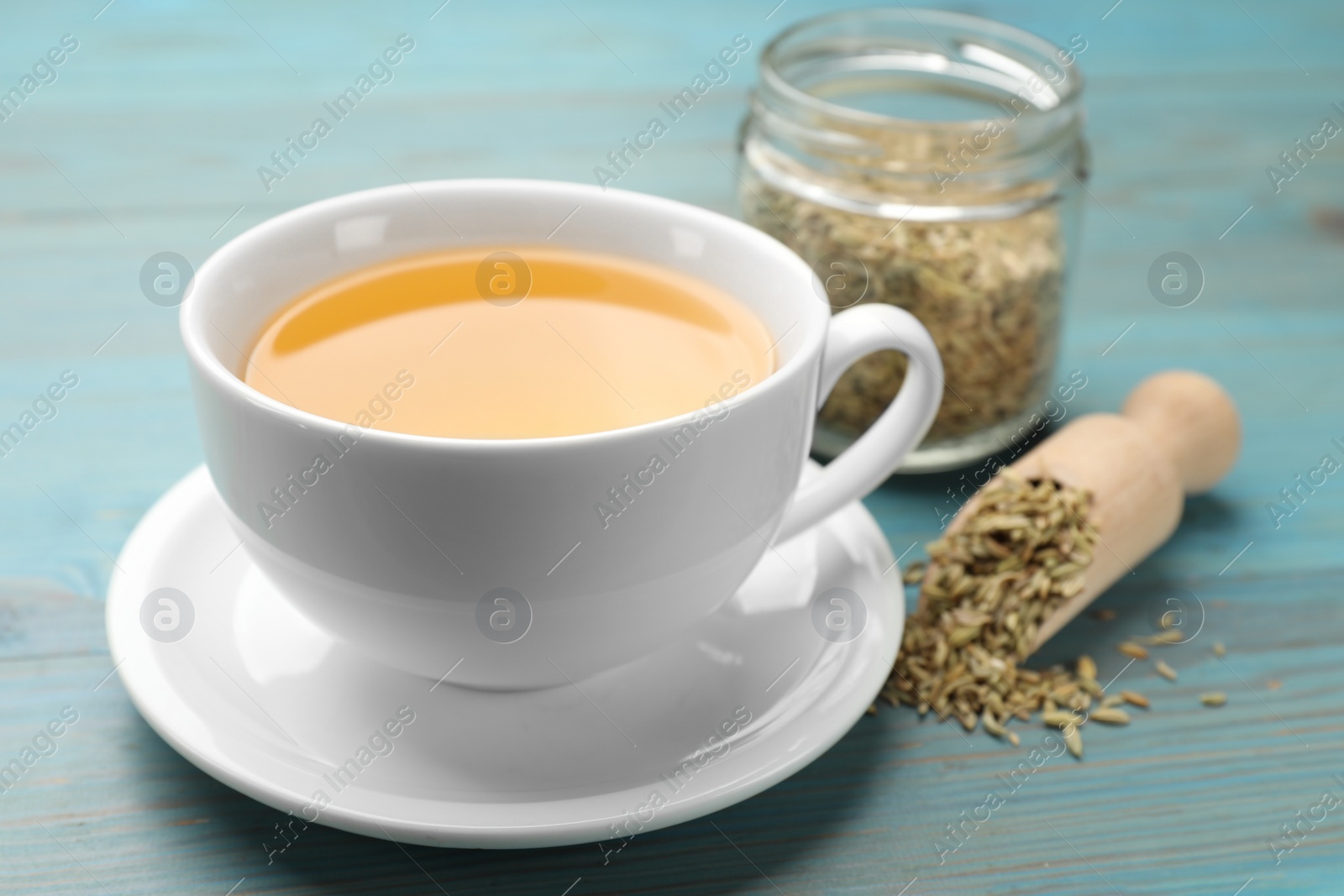 Photo of Fennel tea in cup and seeds on light blue wooden table, closeup