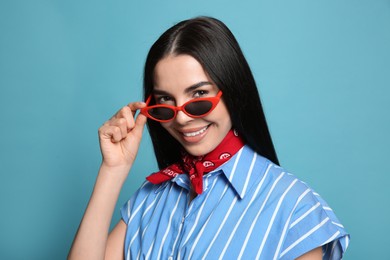 Fashionable young woman in stylish outfit with bandana on light blue background