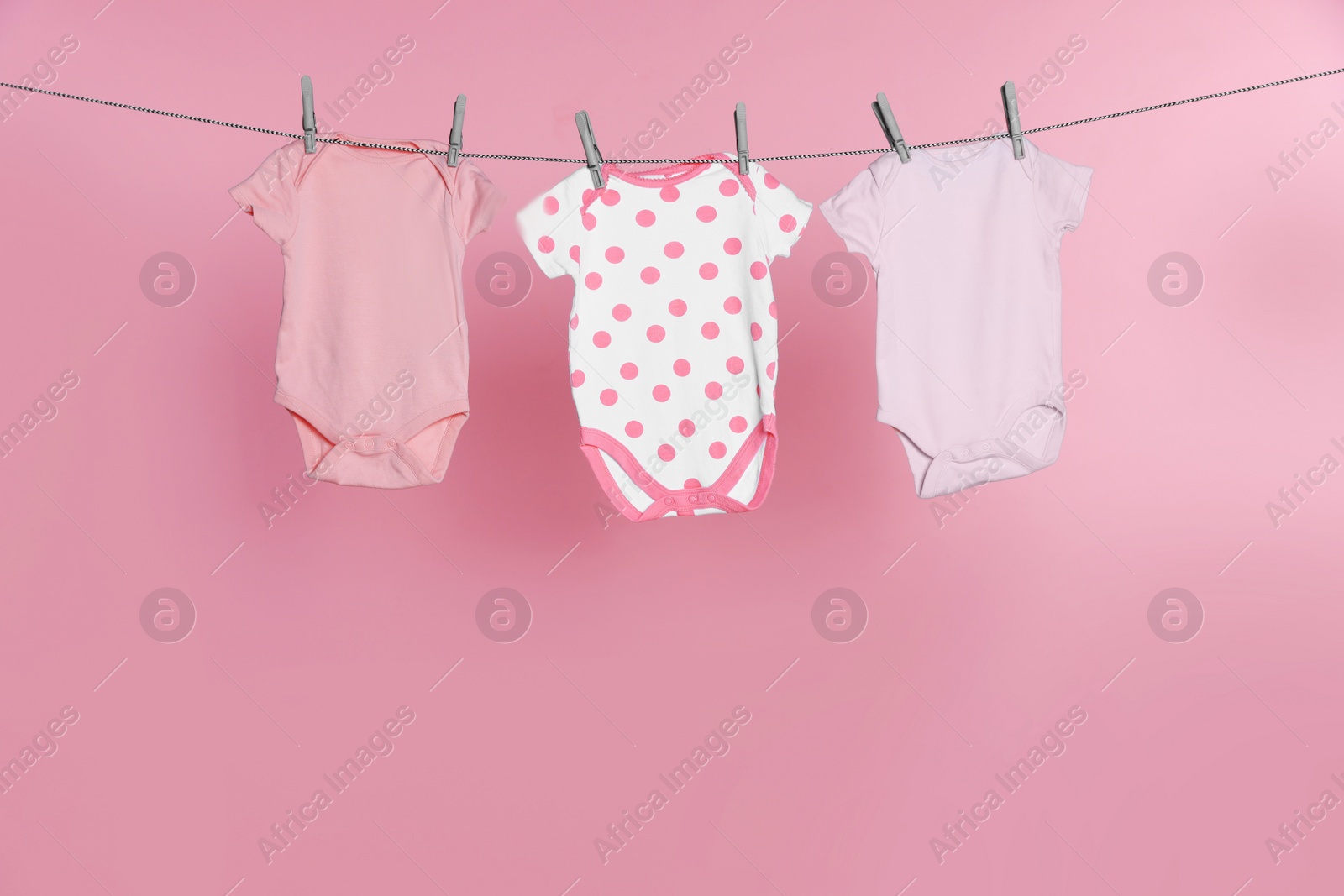 Photo of Baby onesies drying on laundry line against pink background