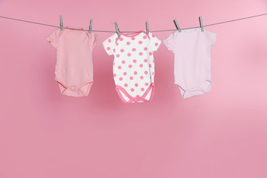 Photo of Baby onesies drying on laundry line against pink background