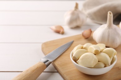 Photo of Fresh garlic and knife on white wooden table, closeup. Space for text