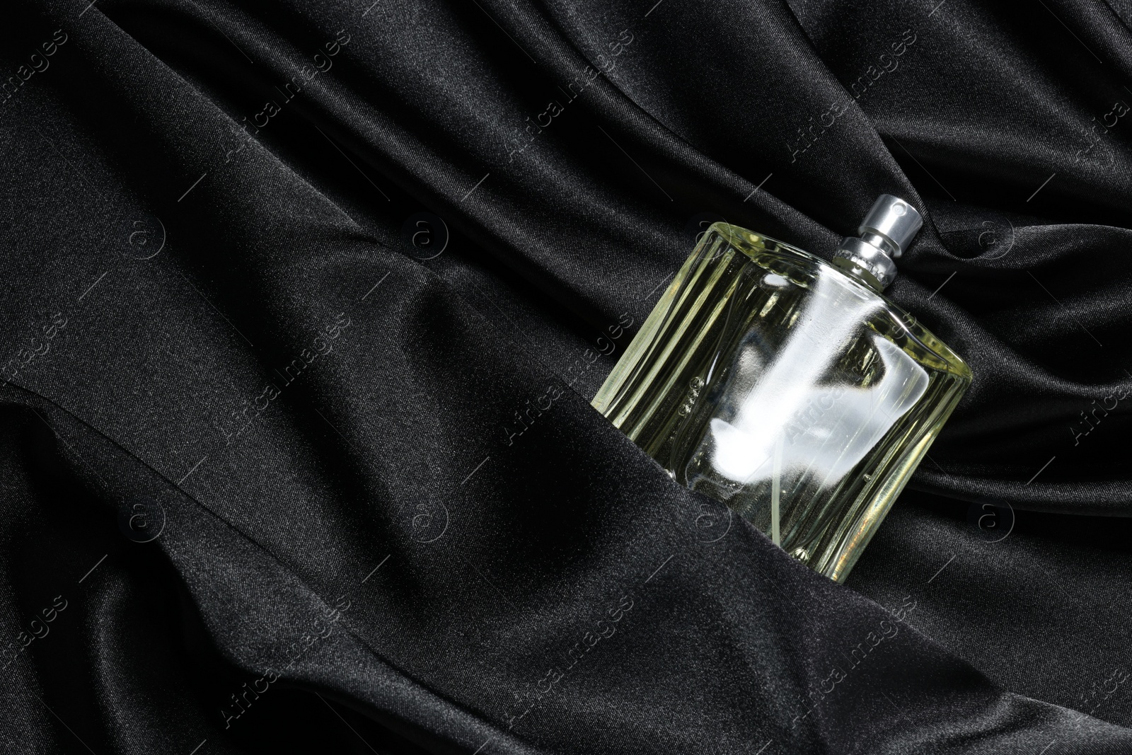 Photo of Luxury men's perfume in bottle on black satin fabric, top view. Space for text