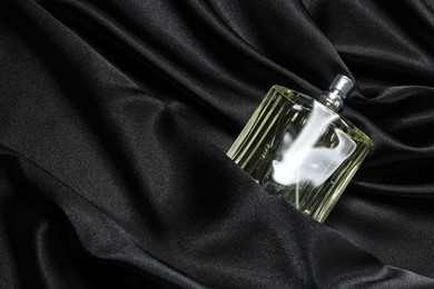 Luxury men's perfume in bottle on black satin fabric, top view. Space for text