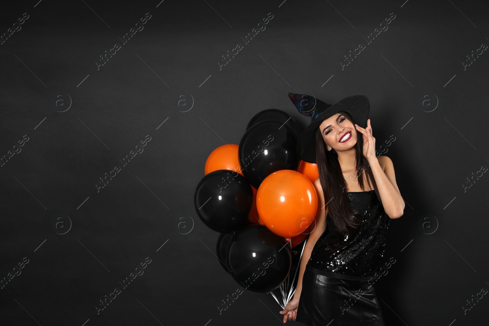 Photo of Beautiful woman wearing witch costume with balloons for Halloween party on black background, space for text