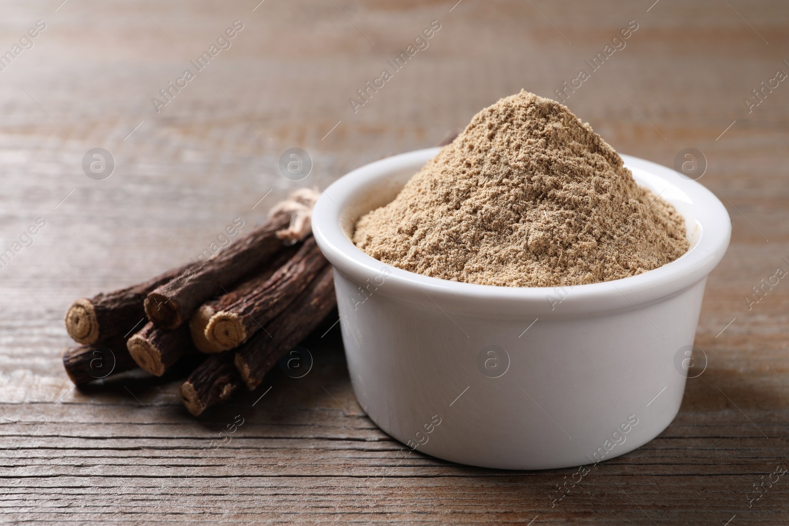 Photo of Powder in bowl and dried sticks of liquorice root on wooden table