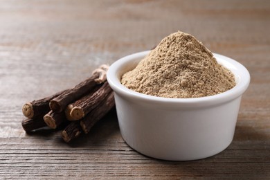 Powder in bowl and dried sticks of liquorice root on wooden table