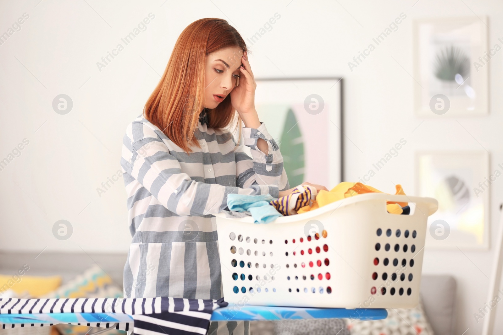 Photo of Tired housewife with basket full of clothes at home