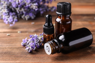 Photo of Bottles with natural lavender oil and flowers on wooden table, closeup view. Space for text