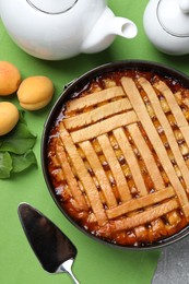 Photo of Delicious apricot pie in baking dish and fresh fruits on table, flat lay