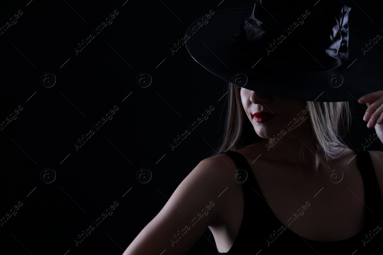 Photo of Young woman wearing witch costume on black background, space for text. Halloween party