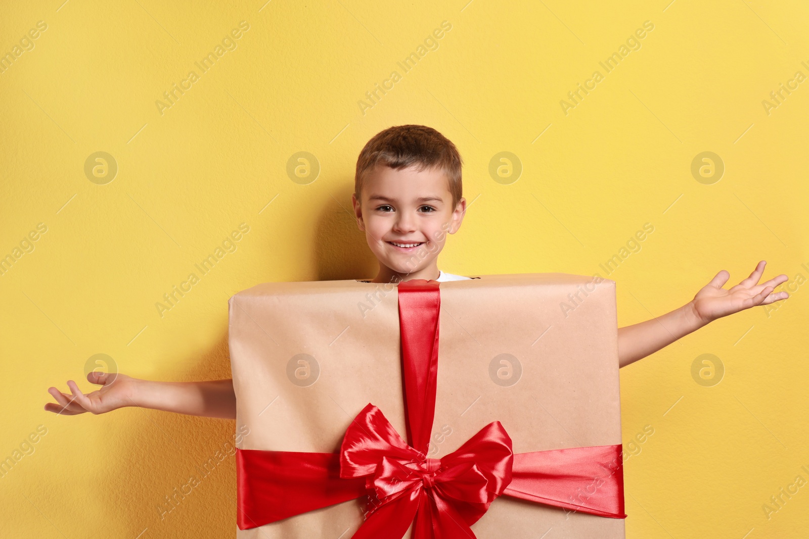 Image of Cute little boy dressed as gift box on yellow background. Christmas suit