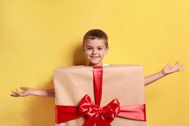 Image of Cute little boy dressed as gift box on yellow background. Christmas suit