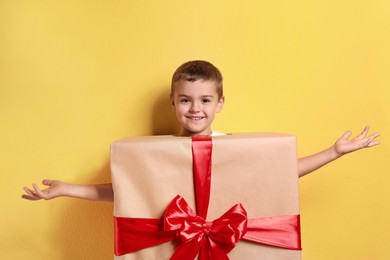 Cute little boy dressed as gift box on yellow background. Christmas suit