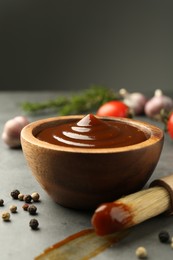 Tasty barbeque sauce in bowl, brush and peppercorns on grey table, closeup