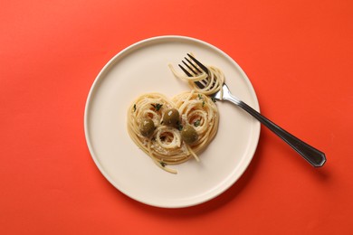 Heart made of tasty spaghetti, fork, olives and cheese on coral background, top view