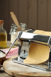 Pasta maker with raw dough on wooden table, closeup