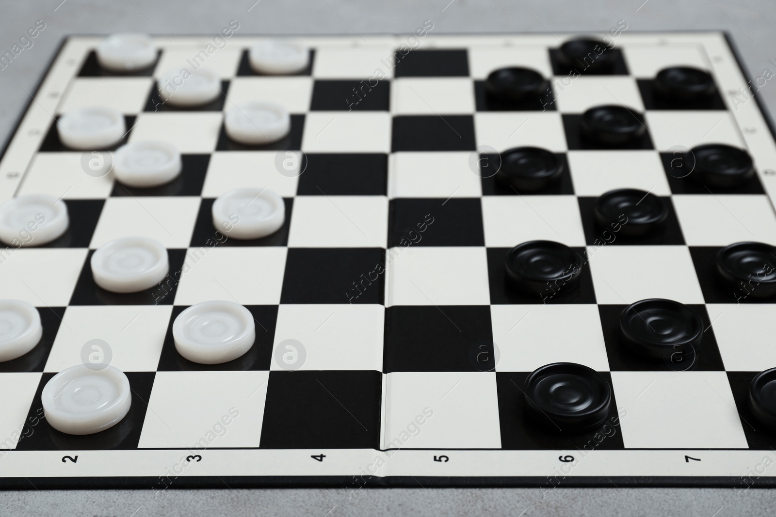 Photo of Checkerboard with game pieces on light grey table, closeup