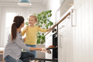 Photo of Mother and daughter taking out buns from oven in kitchen