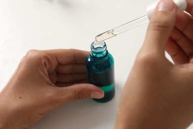 Woman with bottle of cosmetic serum at white table, closeup