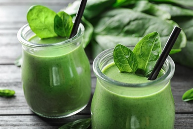 Photo of Jars of healthy green smoothie with fresh spinach on grey wooden table, closeup