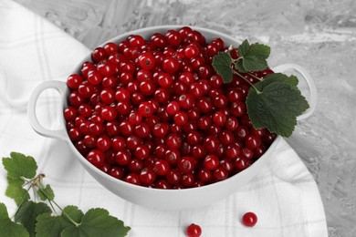 Photo of Ripe red currants and leaves in colander on grey textured table, closeup