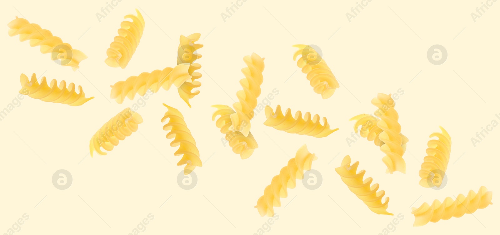 Image of Raw fusilli pasta flying on beige background