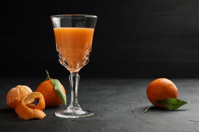 Photo of Tasty tangerine liqueur in glass and fresh fruits on black textured table. Space for text