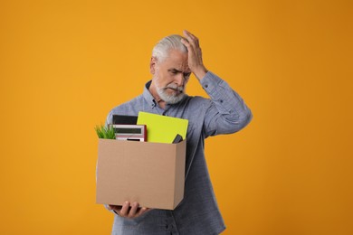 Photo of Unemployed senior man with box of personal office belongings on orange background