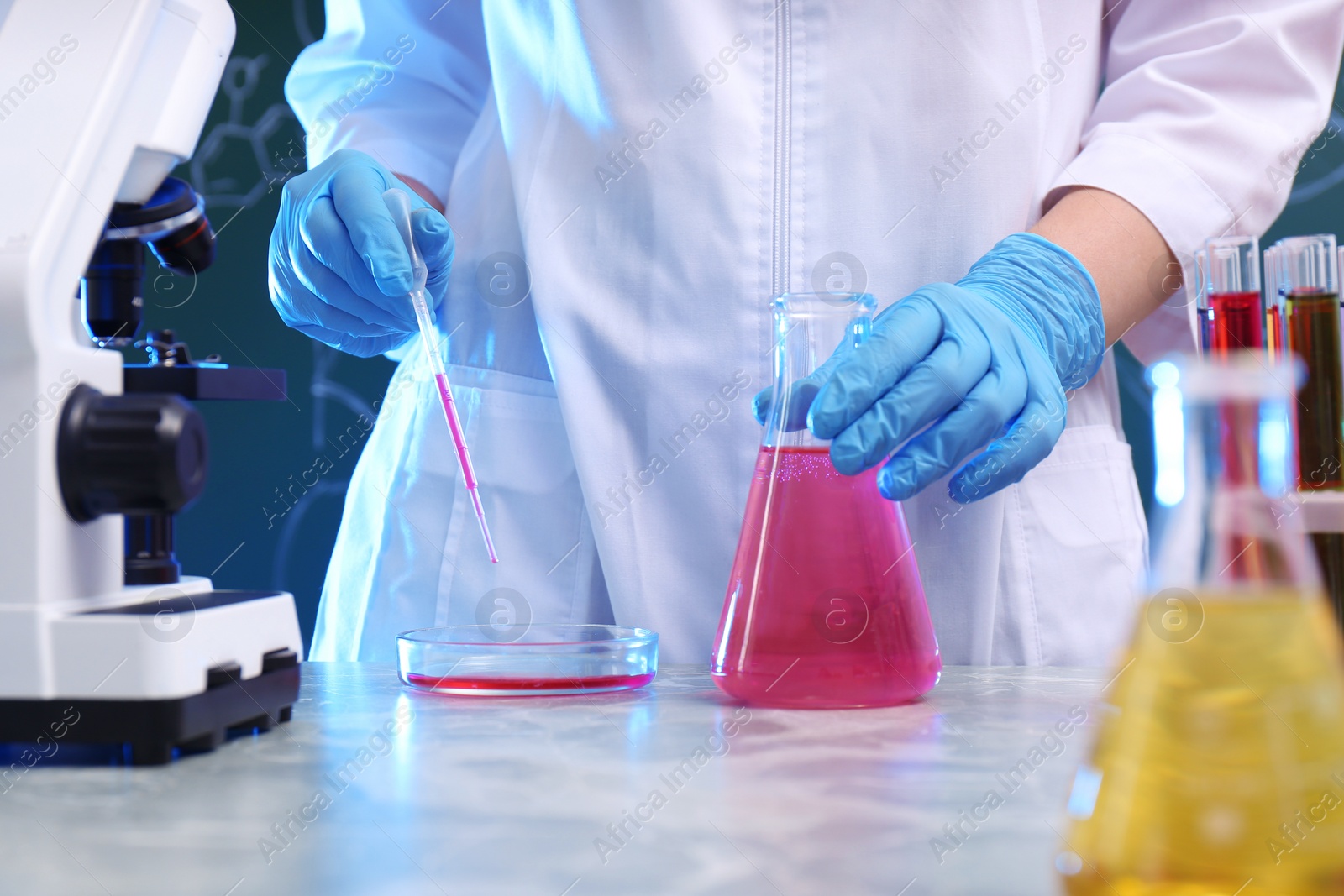 Photo of Scientist taking sample of liquid with dropper at table, closeup. Chemistry glassware