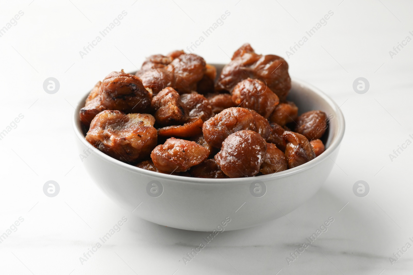 Photo of Roasted edible sweet chestnuts in bowl on white marble table, closeup