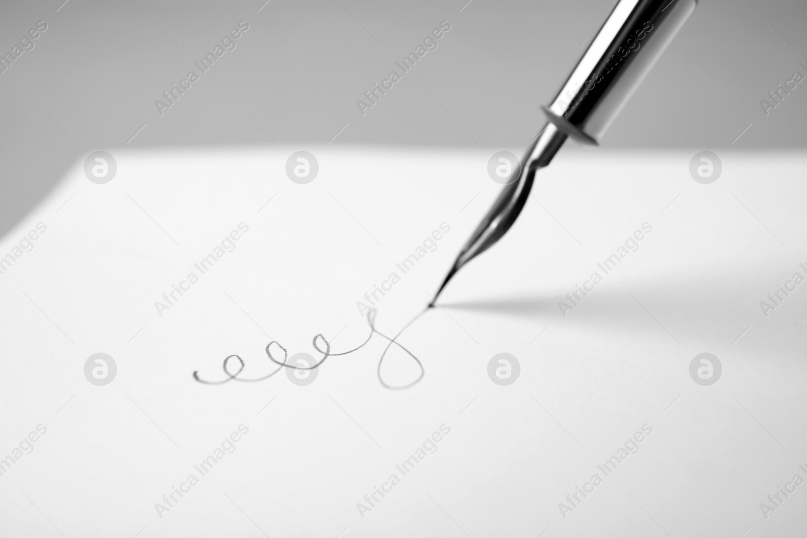 Photo of Signing on sheet of paper with fountain pen against light grey background, closeup. Space for text