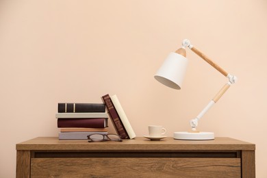 Photo of Books, glasses and lamp on wooden table near beige wall