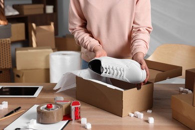 Photo of Seller packing shoes into cardboard box at table in office, closeup. Online store