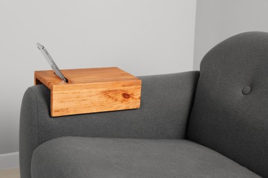 Smartphone on sofa with wooden armrest table in room. Interior element