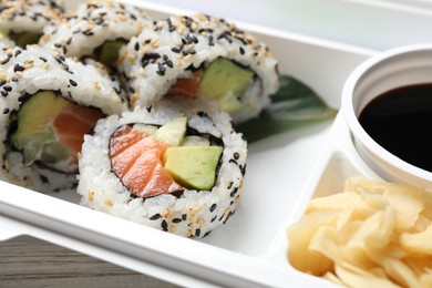 Food delivery. Delicious sushi rolls, soy sauce and ginger in plastic container on table, closeup