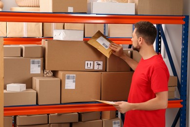 Photo of Post office worker holding adhesive paper bag near rack with parcels indoors