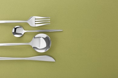 Photo of Fork, knife and spoons on green background, flat lay with space for text. Stylish cutlery set