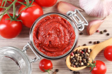 Photo of Jar of tasty tomato paste and ingredients on wooden table, flat lay