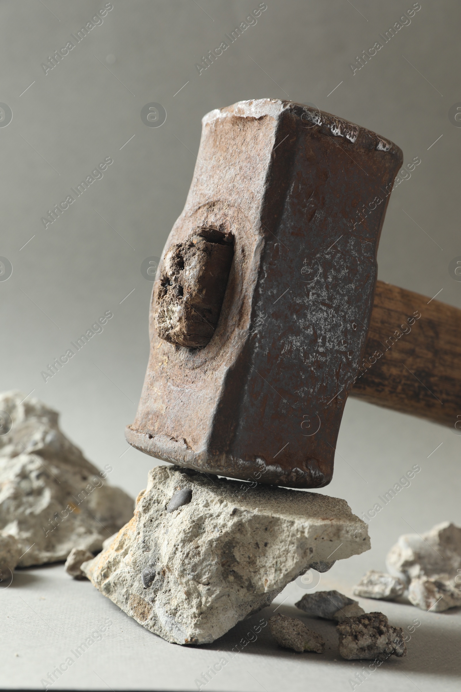 Photo of One sledgehammer and pieces of broken stones on grey background, closeup