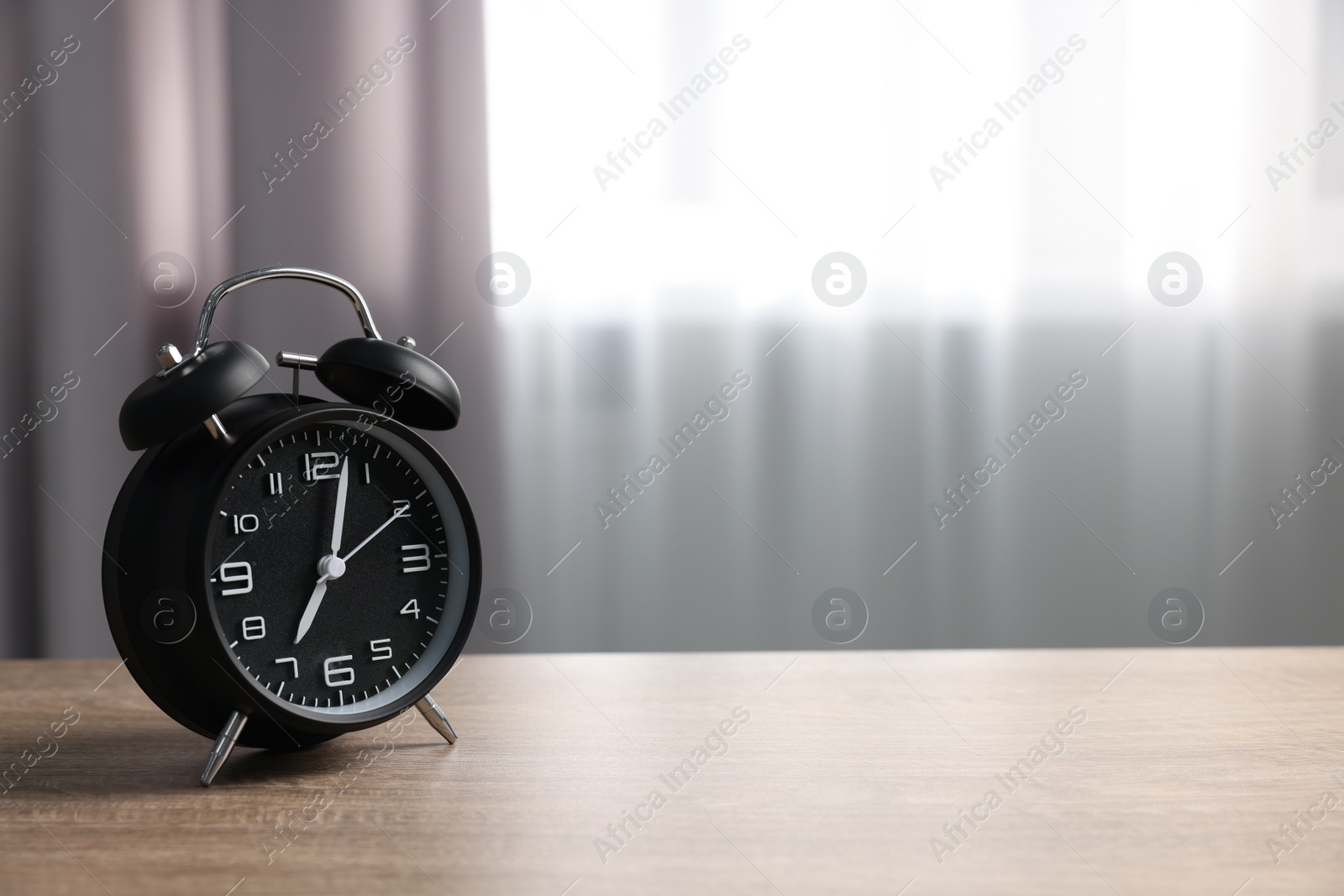 Photo of Black alarm clock on wooden table indoors, space for text